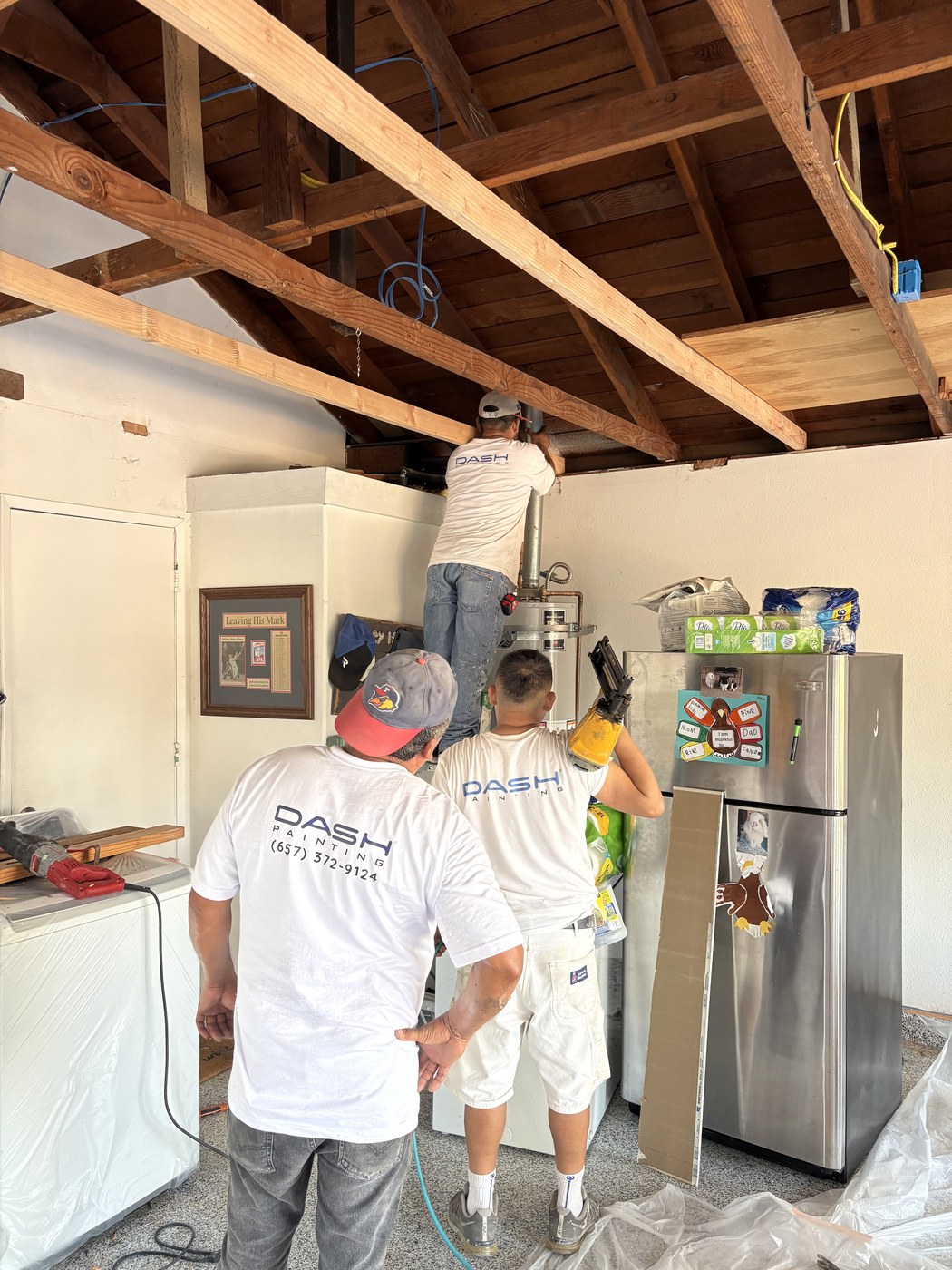 Dash Renovation crew in Dash-branded shirts working on ceiling framing and a water heater during a garage remodel